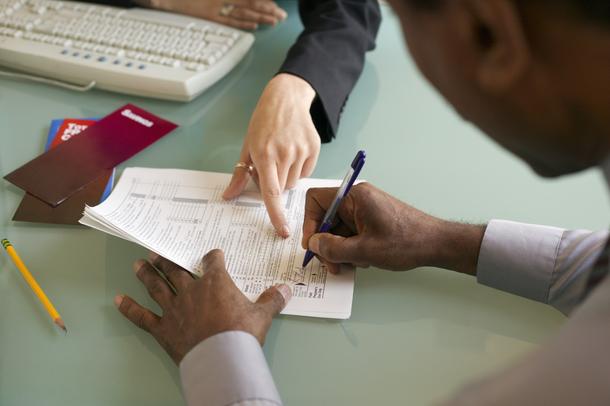 76755235.jpg Two people reviewing and signing documents at a desk, with a keyboard, envelopes, and a pencil nearby.