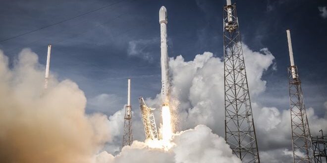 A rocket launches into a cloudy sky, surrounded by launch towers, leaving a trail of smoke and fire.
