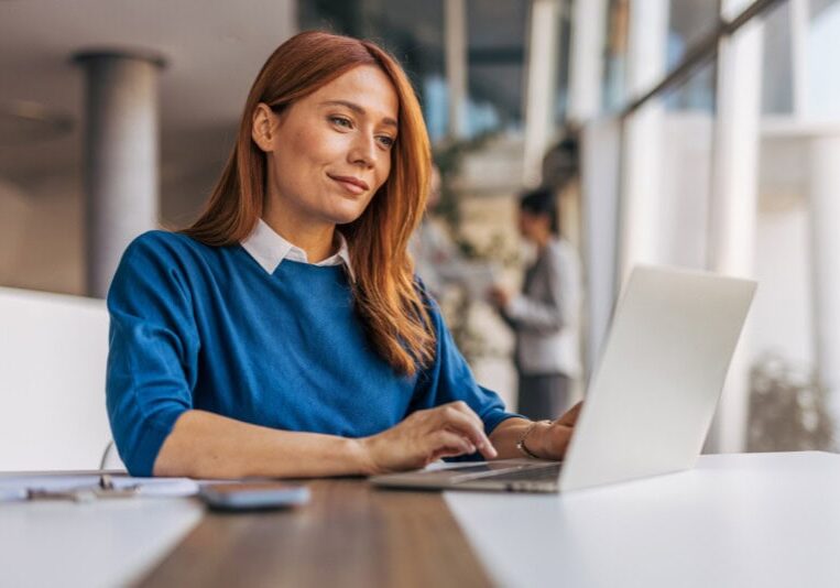 A woman with red hair works on a laptop doing real time expense automation