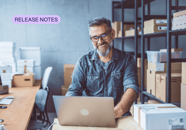 A man with glasses and a beard works on GL-coding at his laptop in a warehouse or office space with shelves of boxes; a "Release Notes" label appears in the corner.