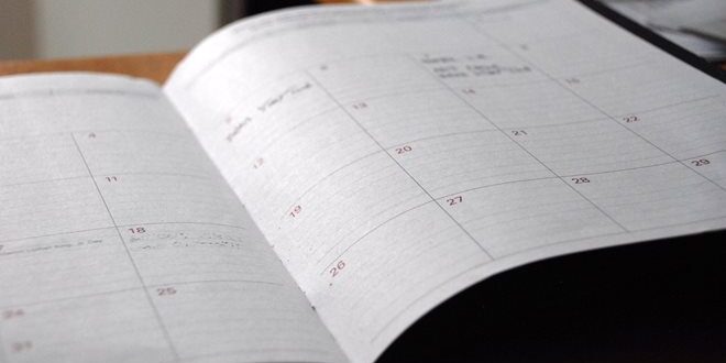 Open planner on a wooden desk displaying a monthly calendar with blank spaces.