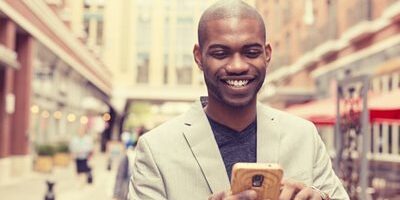 Man in a suit smiling while using a smartphone on a city street.