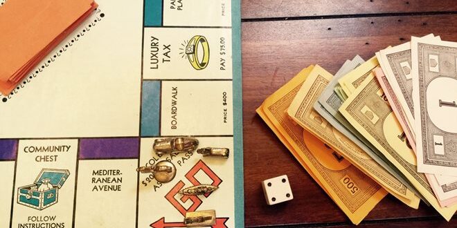 A Monopoly board with dice, tokens, Community Chest cards, and organized play money on a wooden table.