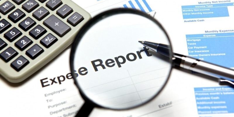 A magnifying glass focuses on an expense report, surrounded by a calculator, a pen, and financial documents.
