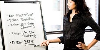 A woman points to a schedule on a flip chart listing times and events from 8:00 a.m. to a 10:30 a.m. break.