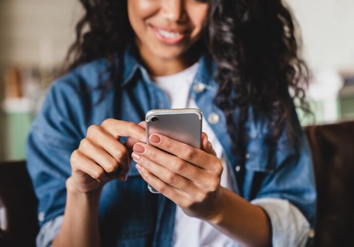 Cropped shot of an african-american young woman using smart phone at home.Smiling african american woman using smartphone at home, messaging or browsing social networks while relaxing on couch