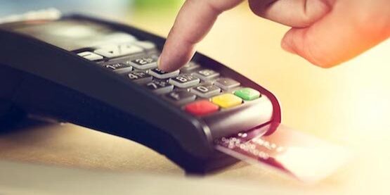 A hand entering a PIN on a card reader with a credit card inserted.