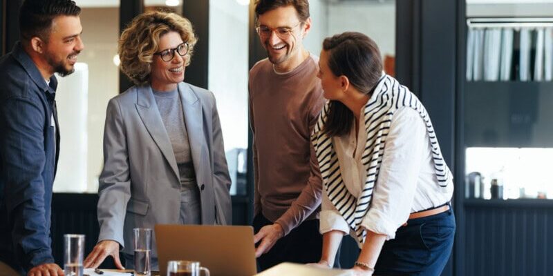 Four people gather around a table, engaged in conversation about the latest expense reporting software and the increased purchasing power to grow their business.