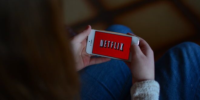 Person holding a smartphone displaying the Netflix logo on the screen.