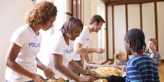 Volunteers distribute meals to children in a dining area.