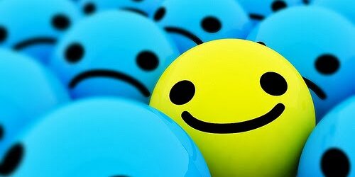 A yellow smiley face ball stands out among a group of blue sad-faced balls.