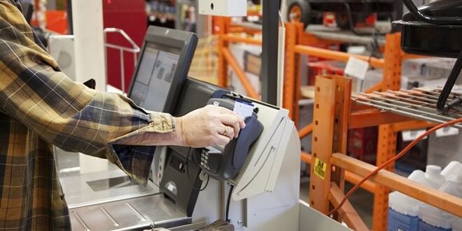 Person using a credit card at a self-checkout machine in a hardware store.
