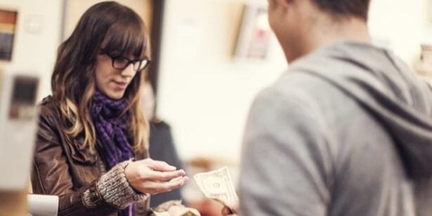 A woman hands money to a cashier at a checkout counter.