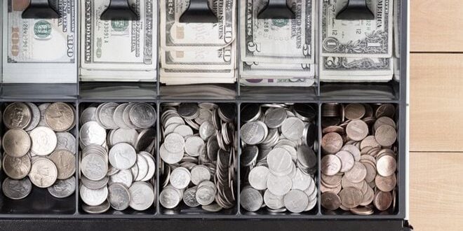 Cash register drawer with U.S. currency: bills in various denominations stacked in back and coins sorted by type in front compartments.