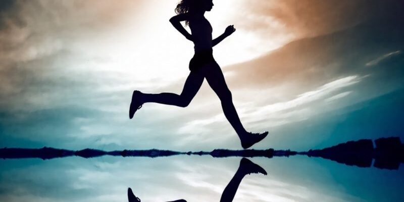 Silhouette of a person running along a reflective surface with a colorful sky in the background.