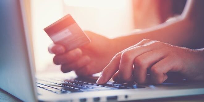 Person holding a credit card while typing on a laptop keyboard, suggesting online shopping or payment.