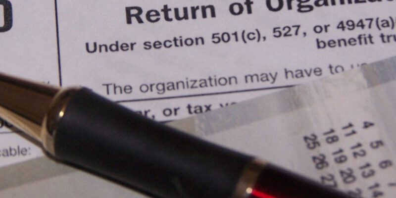 A pen rests on tax documents, including a form related to section 501(c) for business entities and organizations.