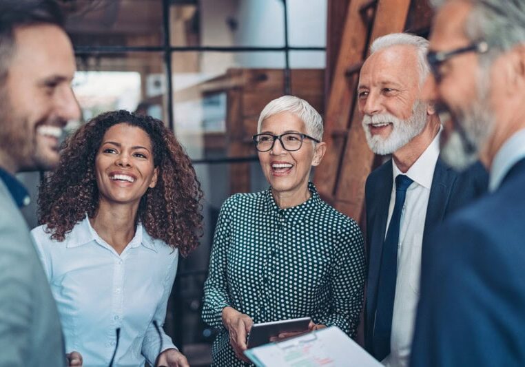 Five professionally dressed people stand together indoors, smiling and talking about top expense management solutions for growing businesses