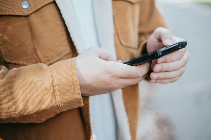 construct-earn Person in a brown jacket holding a smartphone outdoors.