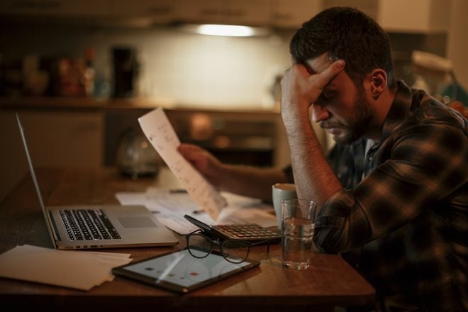 employeestress.jpg A man sits at a table with a laptop and paperwork, holding his head in frustration.