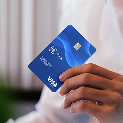 Hand holding a blue PEX Visa card with a chip, featuring logo and text. Background is blurred.