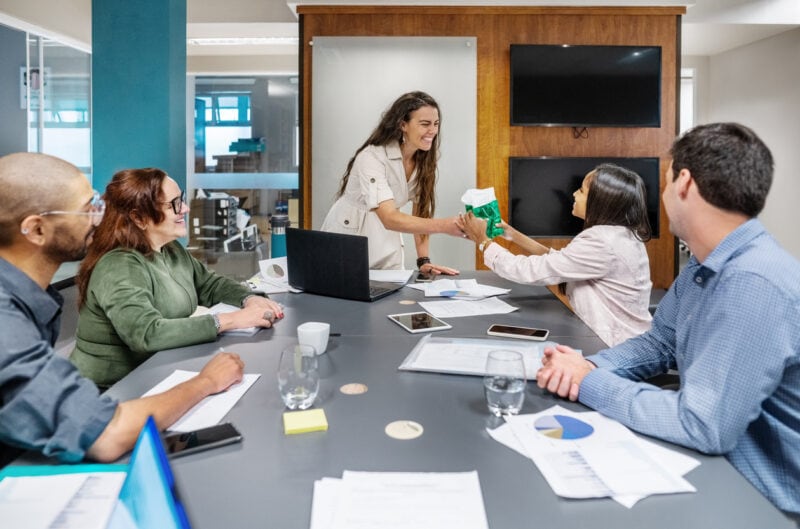 Businesswoman giving gift to female colleague for her best performance during a staff meeting in office conference room