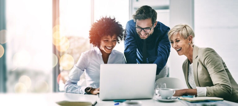 Three people smile while looking at a laptop screen in an office setting, possibly discussing the mysterious allure of ghost cards.