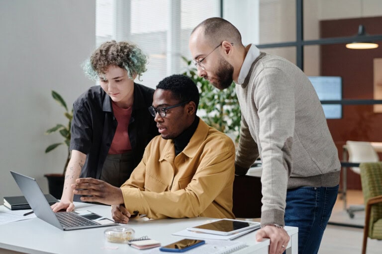 Diverse Group of Office Workers Working in Team on Business Project on Computer Three people collaborate at a desk, intently focused on a laptop screen, discussing their financial priorities.