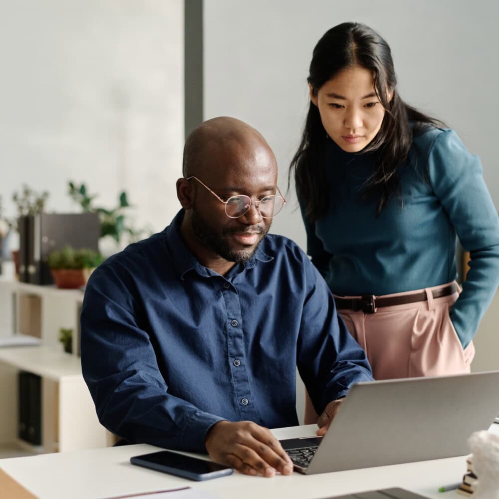 Young African American man working on presentation design on laptop showing it to his Asian coworker, copy space