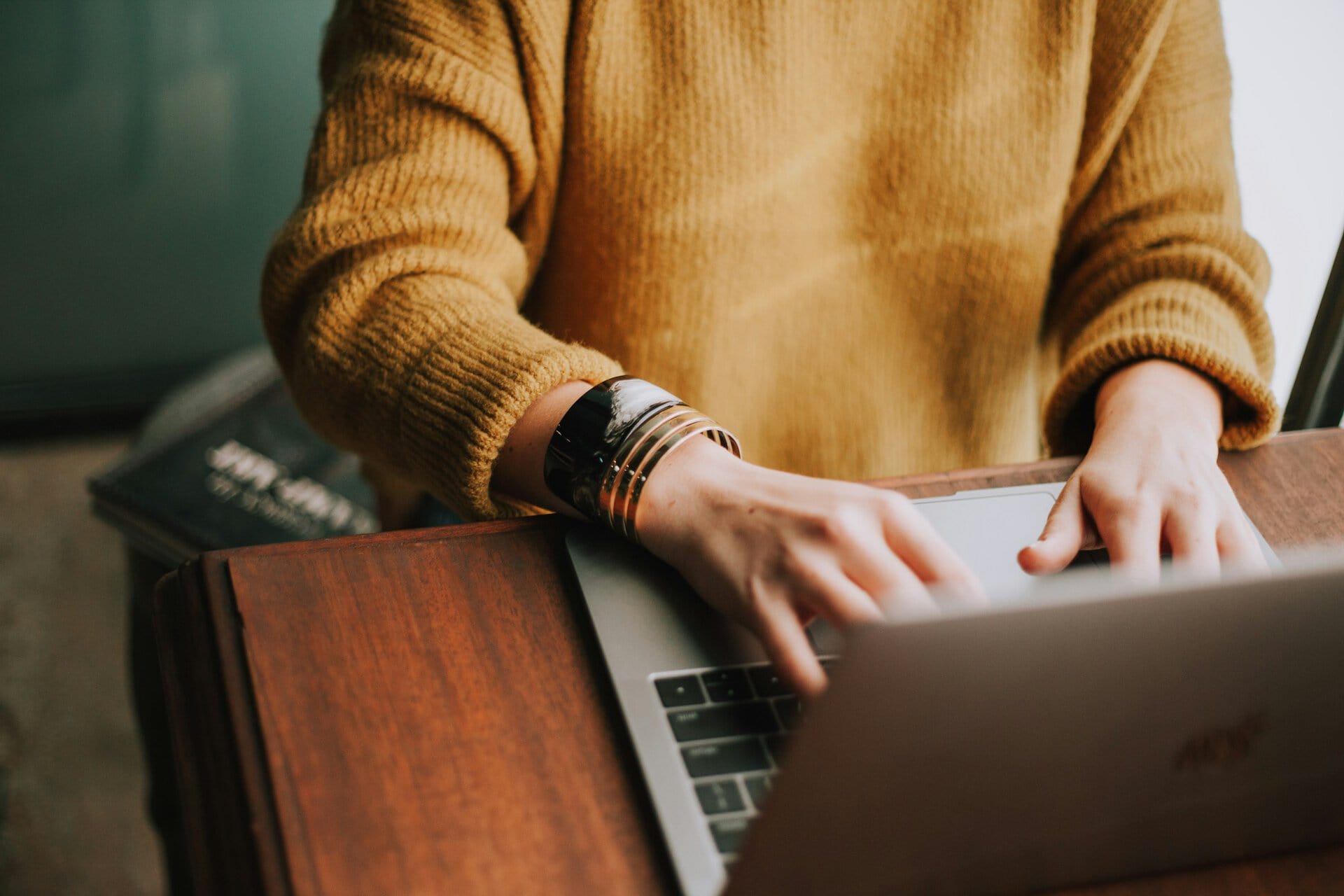 non-profit-director-reconciling-expenses Person in a mustard sweater typing on a laptop at a wooden desk.