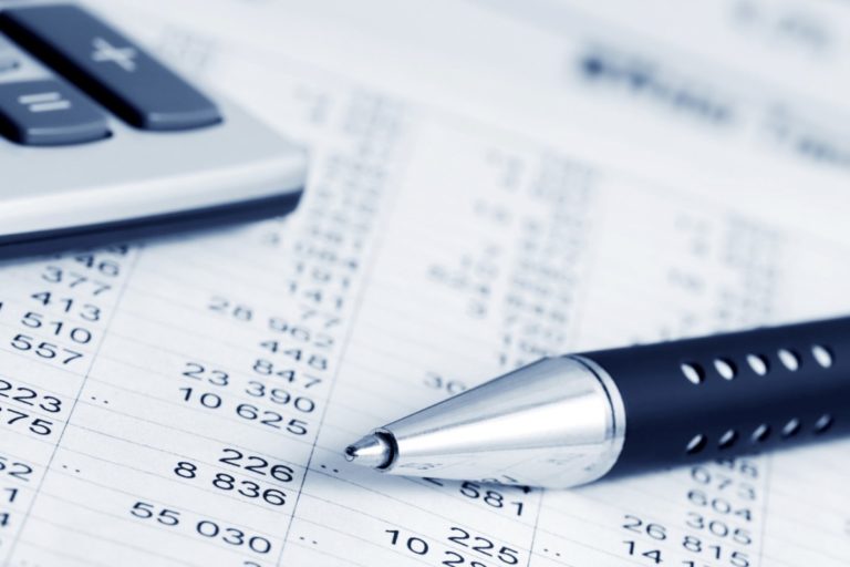 A close-up of a pen, a calculator, and a spreadsheet with numerical data, indicating financial calculations or accounting work.