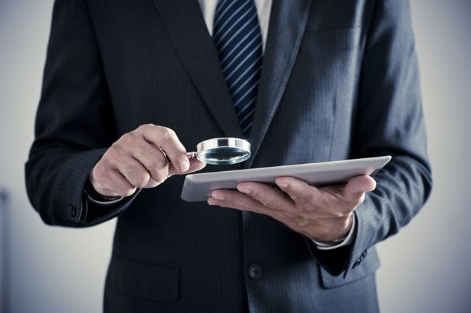 prepaidfraud.jpg A person in a suit examines a tablet closely with a magnifying glass.