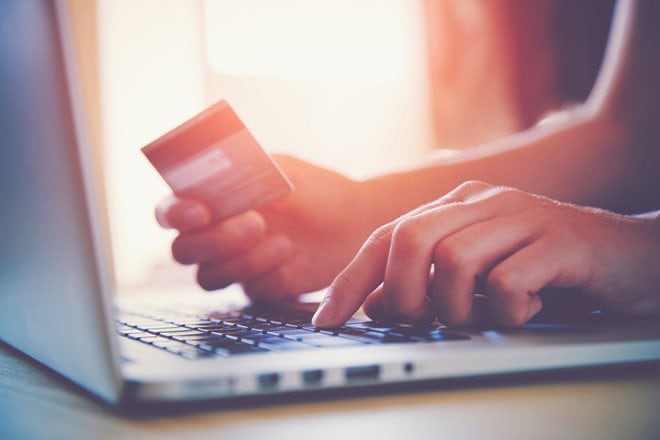 Person holding a credit card while typing on a laptop keyboard, suggesting online shopping or payment.
