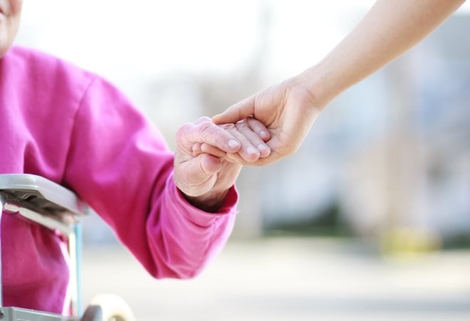 Close-up of two people holding hands, with one person in a wheelchair wearing a pink sweater.