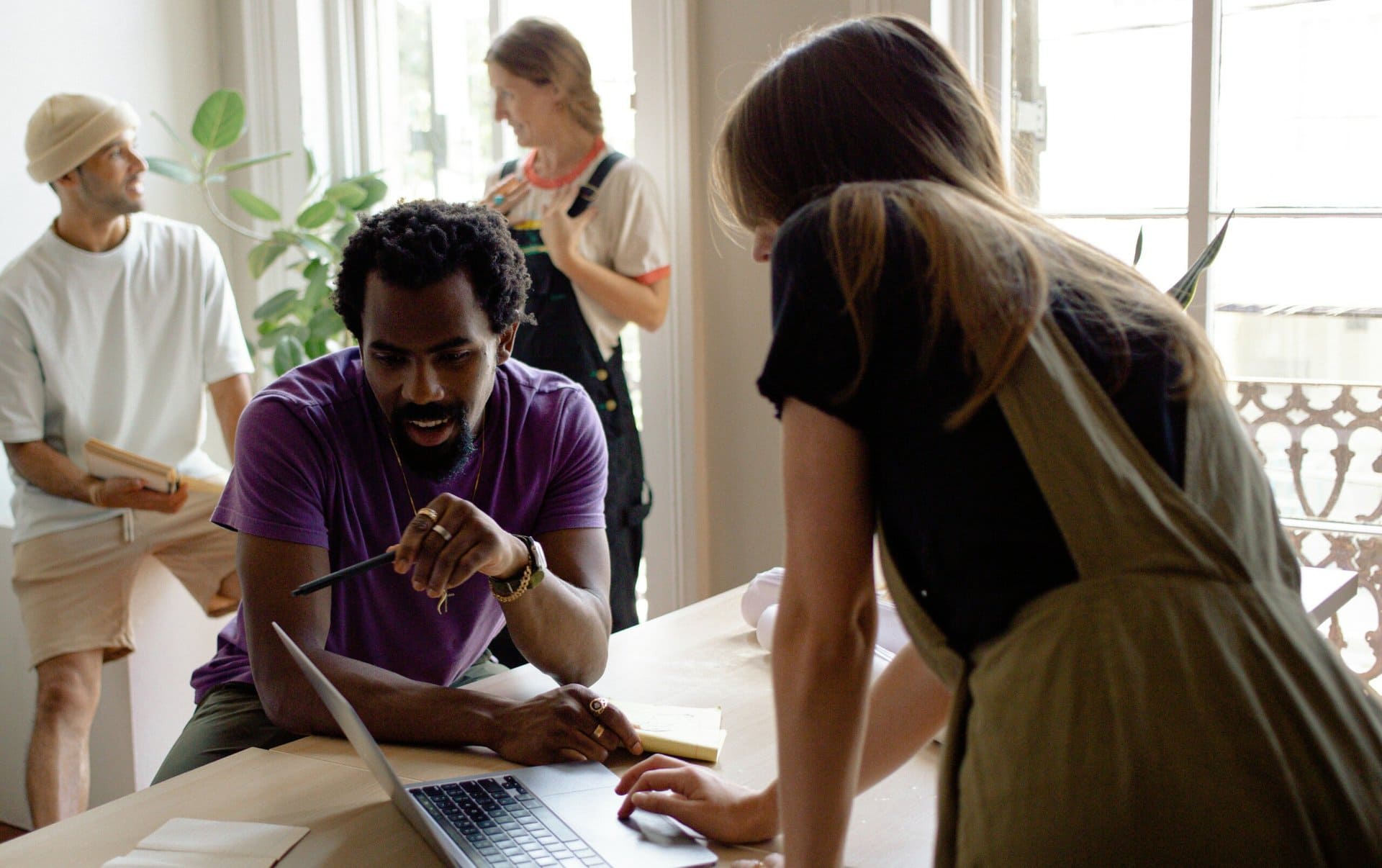 team-working-on-production Four people in a casual office setting are discussing something while looking at a laptop.