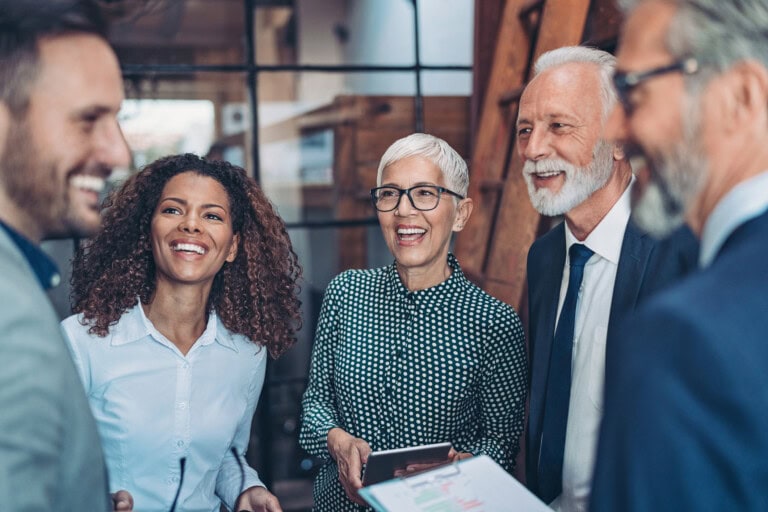 Five professionally dressed people stand together indoors, smiling and talking about top expense management solutions for growing businesses